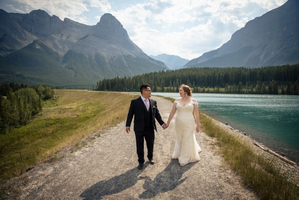 Bride and groom walk hand in hand near a emerald Green lake in Canmore, AB