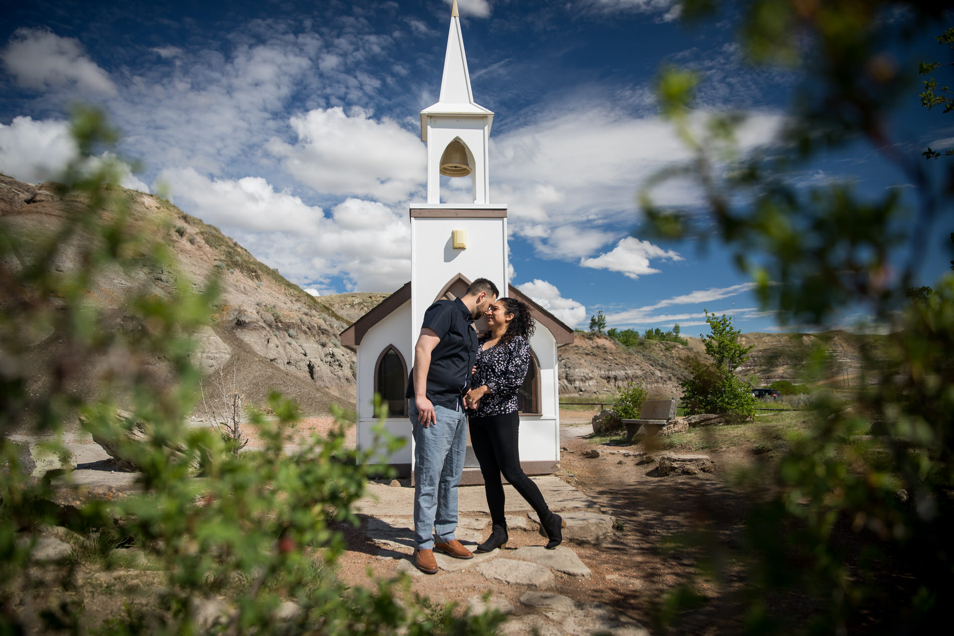Summer photo of engagement couple in Drumheller standing in front of the Little Church