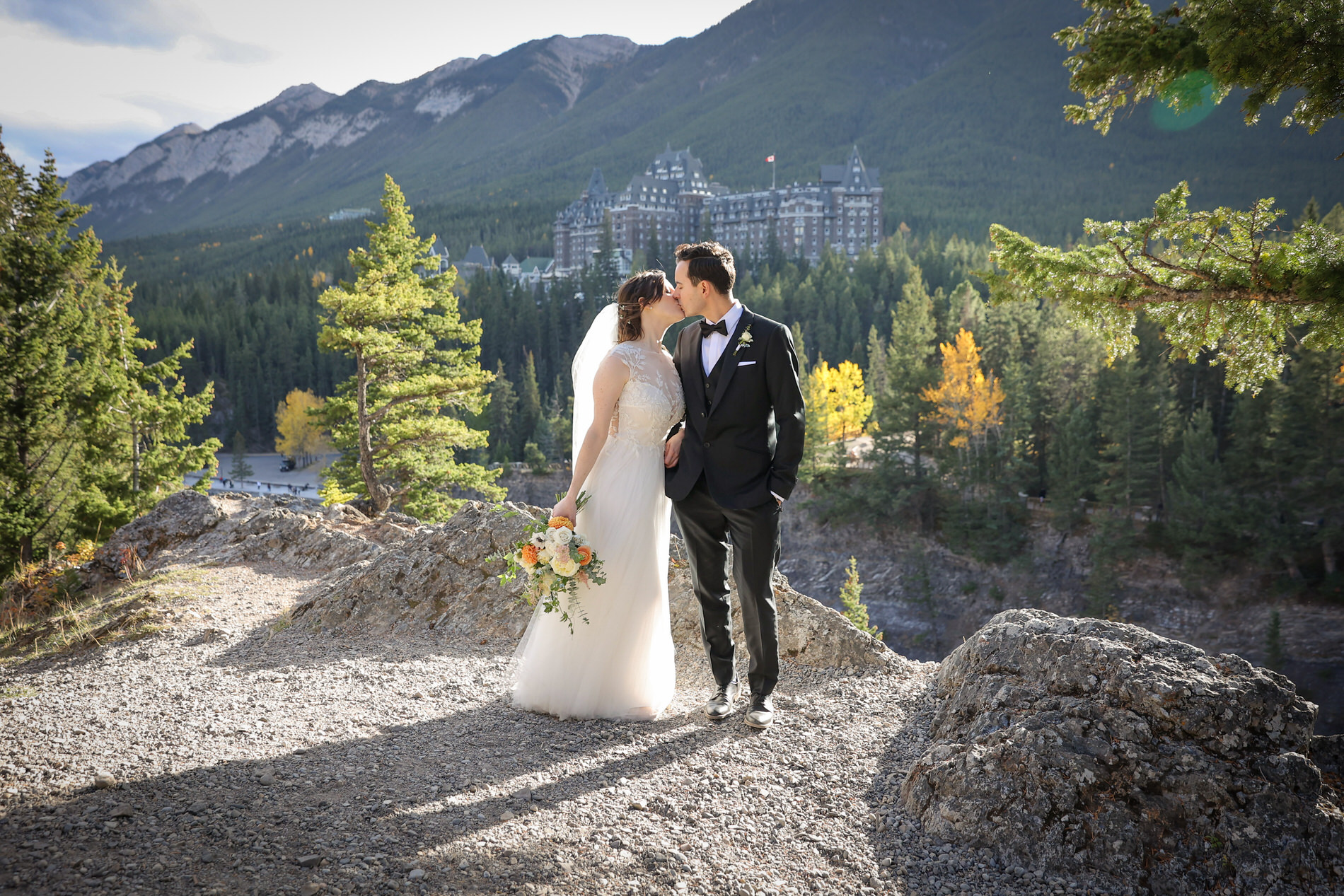 Bride and Groom take wedding photos at Surprise Corner in Banff with Fairmont Hotel in the background