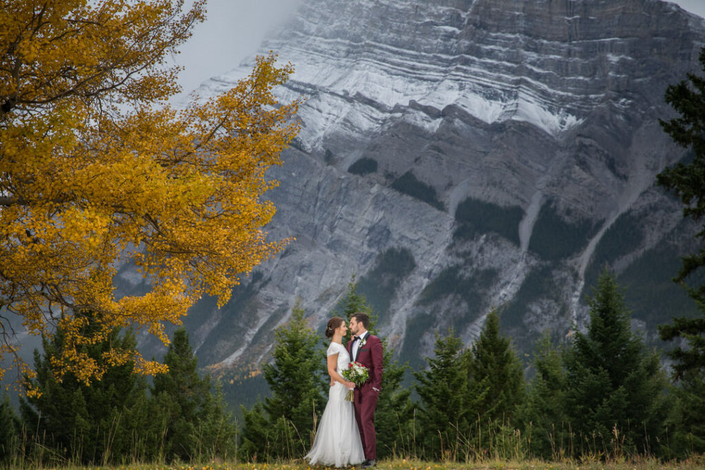 Bride and groom get married in Fall in Banff. They stand in front of Rundle Mountain with fall colour on the trees, and snow on the mountains